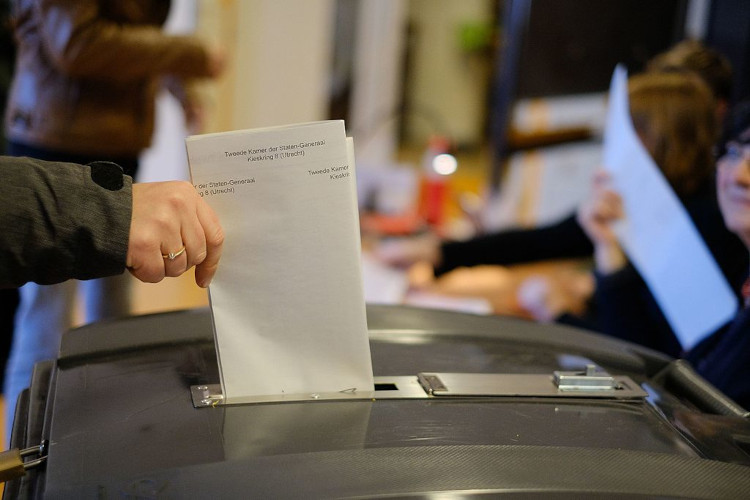 Een foto van een stembiljet die in een stembus wordt gedaan, genomen vanaf de zijkant.